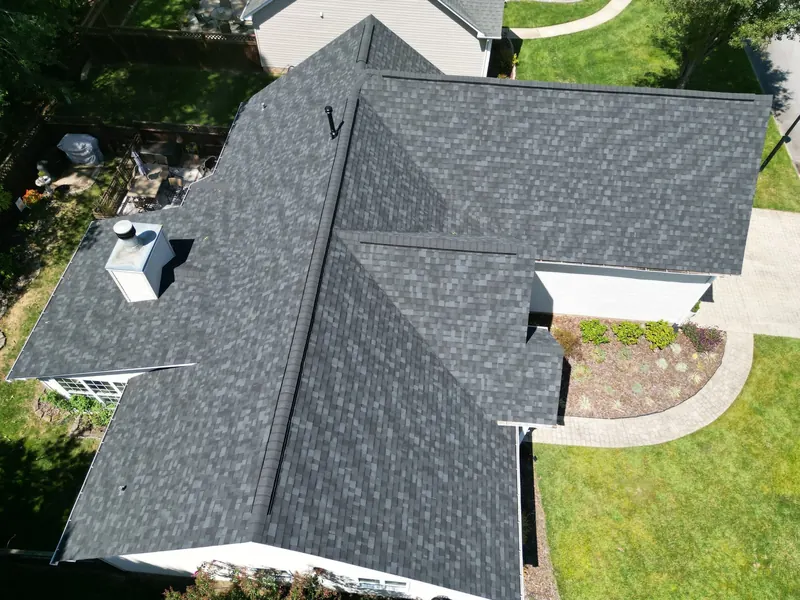 Aerial view of a gray shingle roof on a white home with a chimney and front lawn.